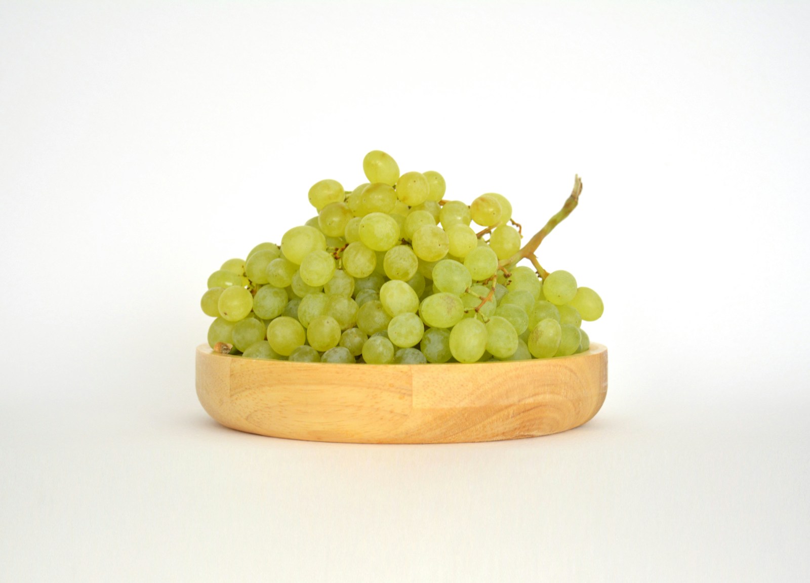 A wooden bowl filled with green grapes